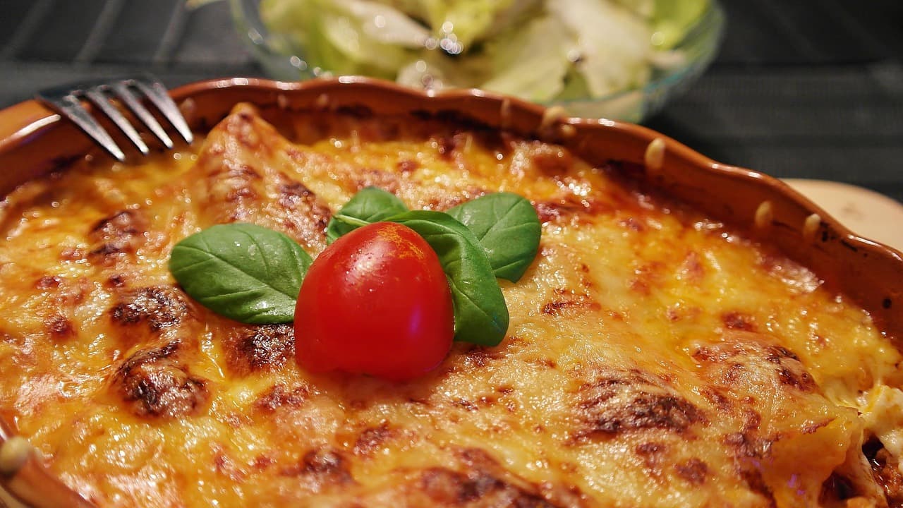 A dish of baked lasagne, golden on top, with basil and a tomato
