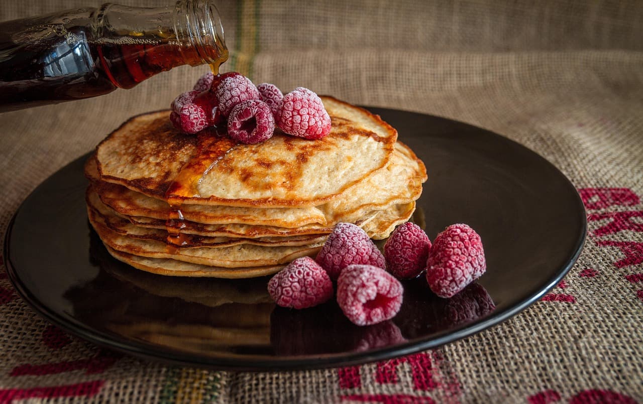 A stack of pancakes with raspberries and syrup