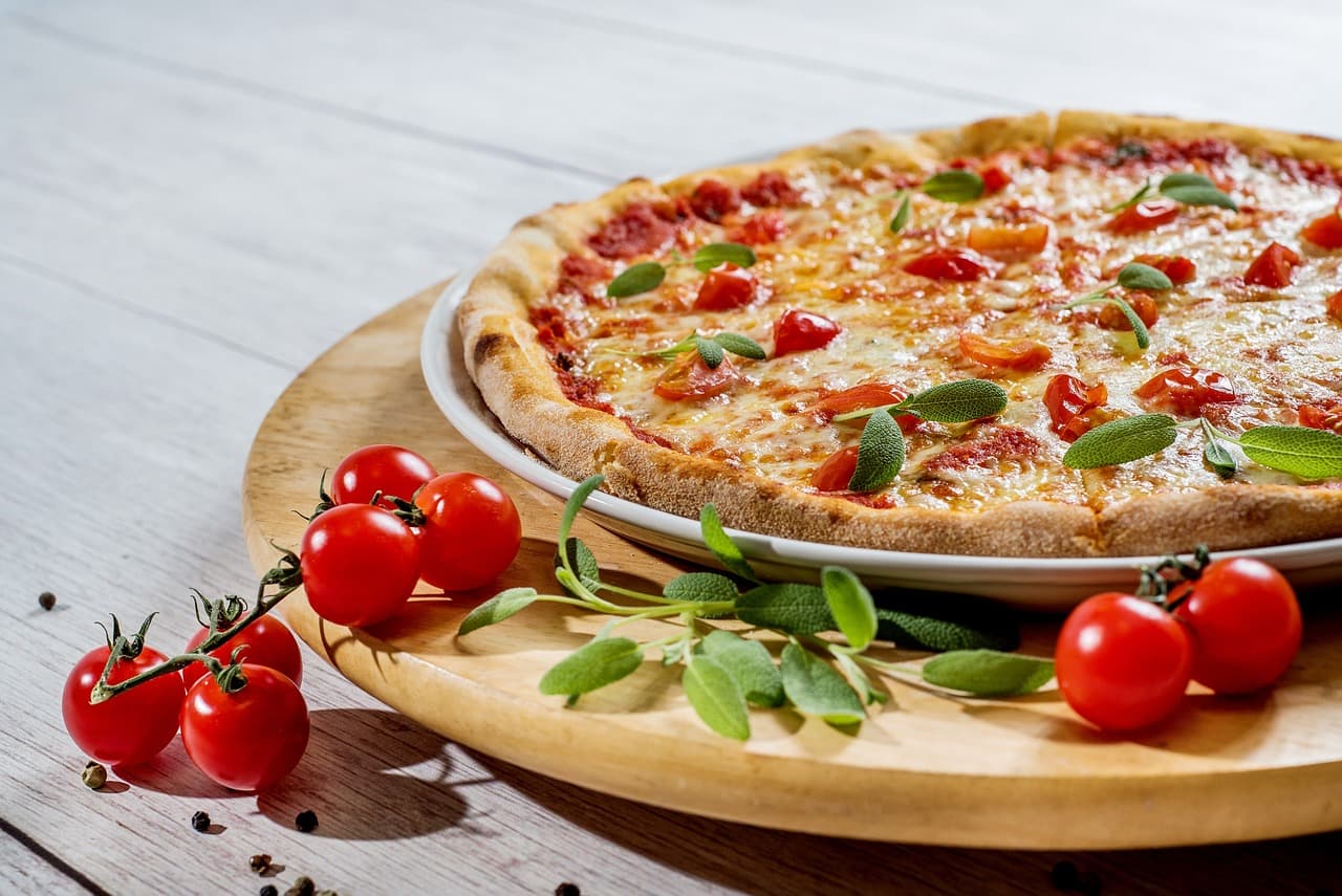 A pizza with tomato and basil on a wooden board, cherry tomatoes beside it