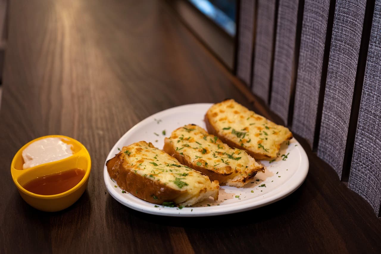 Garlic bread with herbs on a white plate, on a dark wooden table